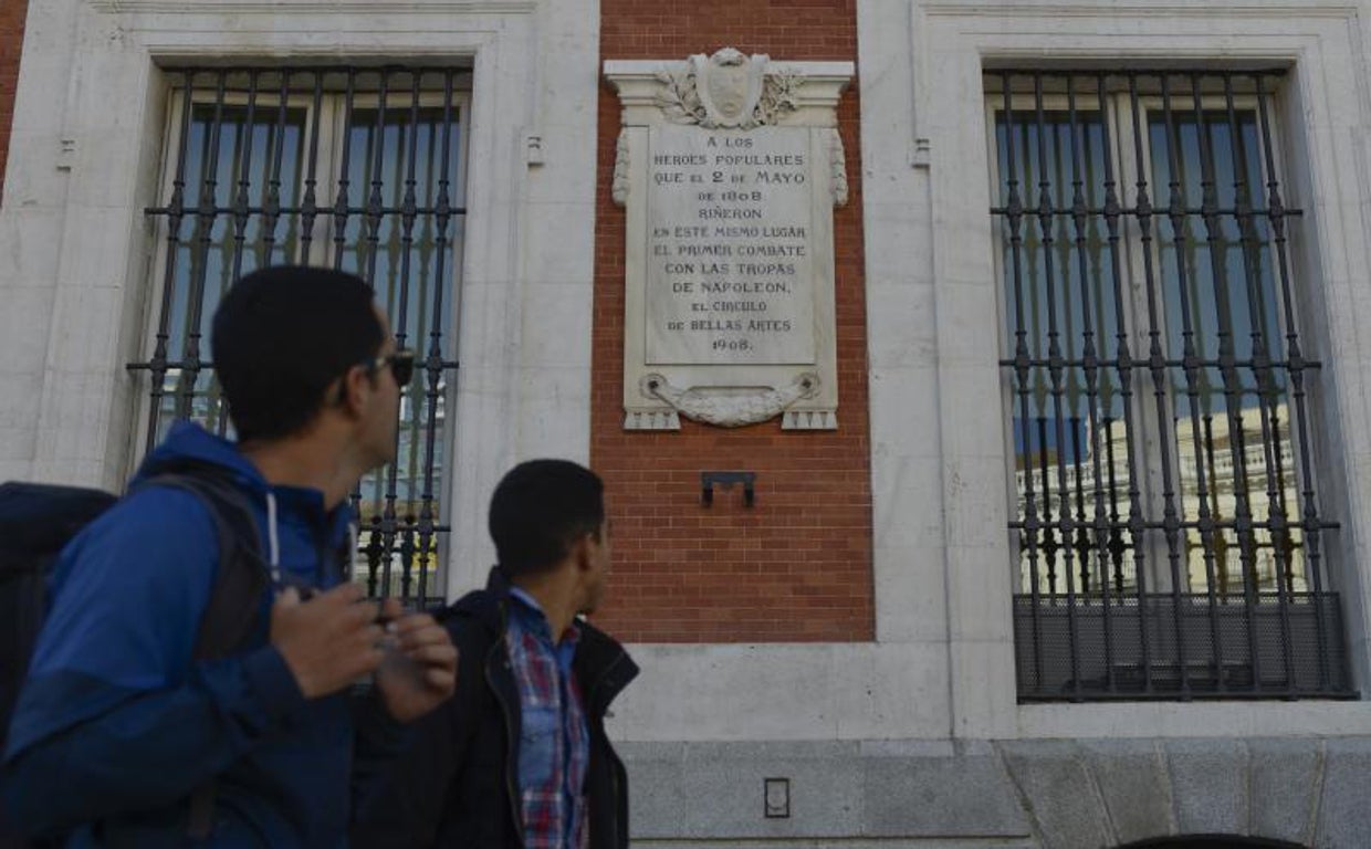 Dos jóvenes pasan junto a la placa dedicada a los héroes del Dos de Mayo, en la Puerta del Sol