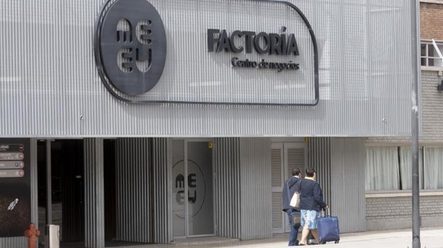 Dos viajeros pasan por delante de la puerta de Factoría MEEU