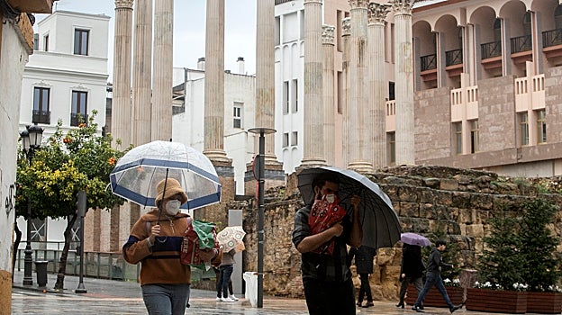 Varias personas pasan por la zona del Templo Romano, en una jornada lluviosa