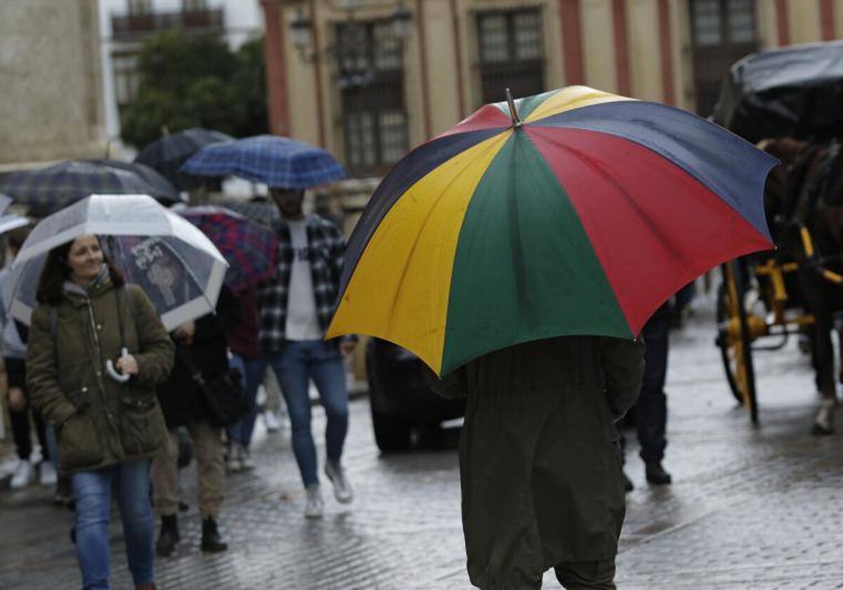 Varias personas se protegen de la lluvia mientras pasean por Sevilla
