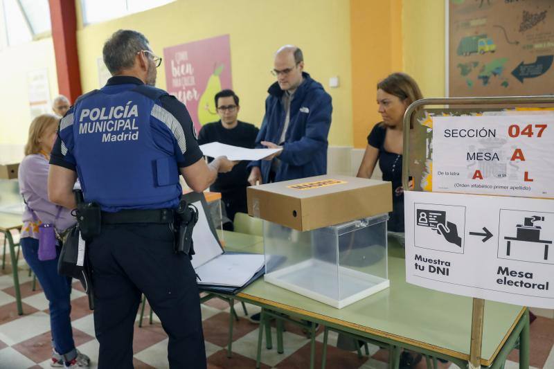 Un policía municipal de Madrid entrega documentación electoral en una de las mesas antes de la apertura de un colegio electoral en Madrid