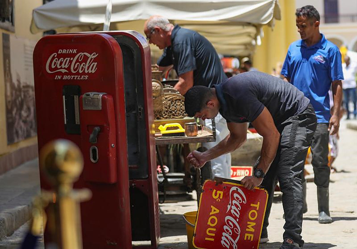 Un hombre limpia una nevera con publicidad de Coca-Cola en una calle de la Habana Vieja, en La Habana (Cuba)