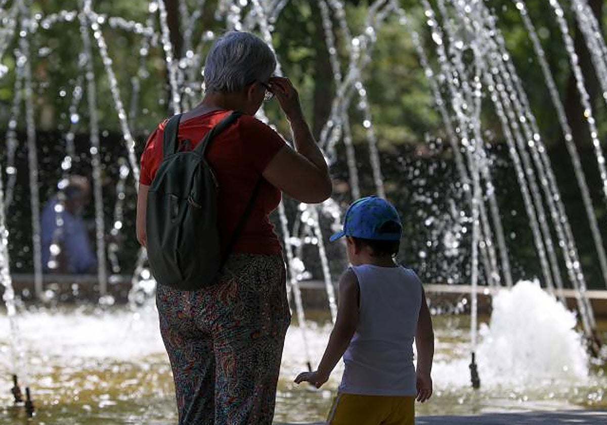 Niños y adultos se refrescan a la sombra, junto a las fuentes públicas del parque del Retiro