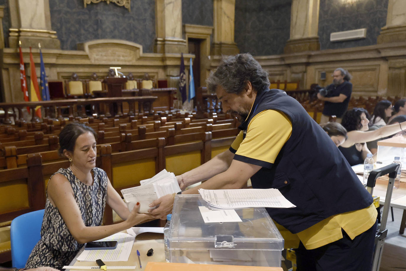 Un cartero que lleva votos por correo llega escoltado por dos agentes de la policía a un colegio electoral de Madrid 