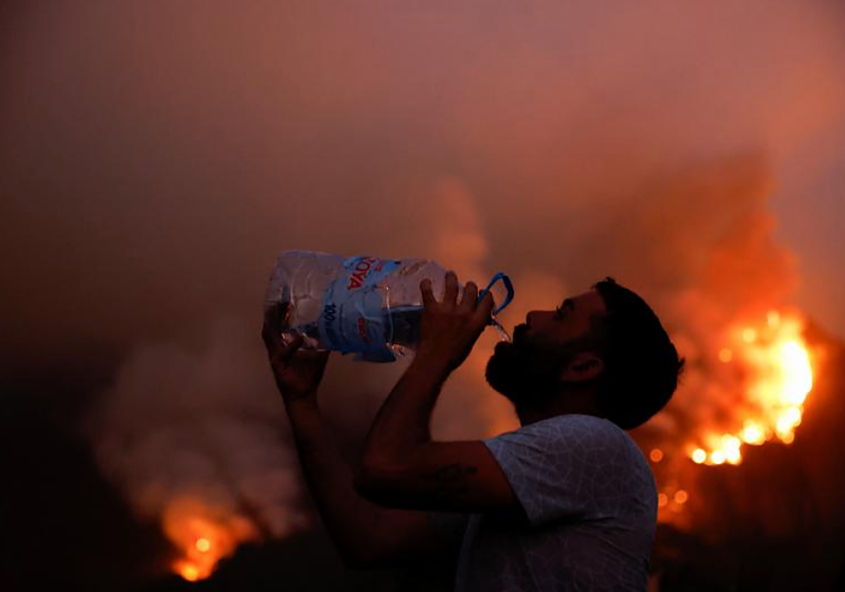 Un vecino de Aguamansa bebe agua frente a uno de los frentes activos del incendio
