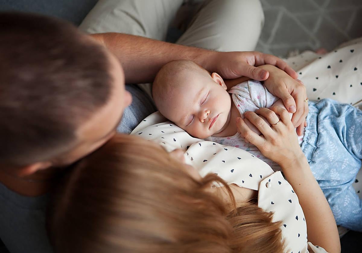 Imagen de archivo de un bebé acurrucado entre los brazos de sus padres