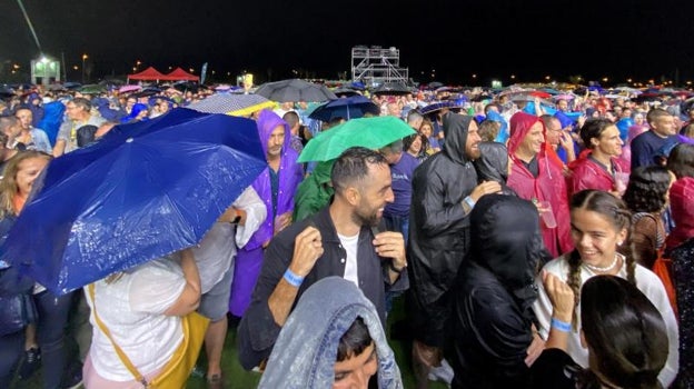 Público con chubasqueros y paraguas bajo la lluvia durante el recital.