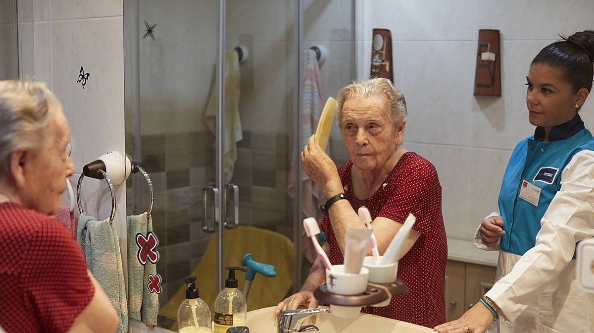Herminia, de 95 años, se peina bajo la supervisión de Sara, la auxiliar de ayuda a domicilio