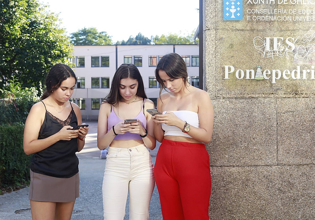 Tres estudiantes consultan sus teléfonos a la entrada de un centro gallego
