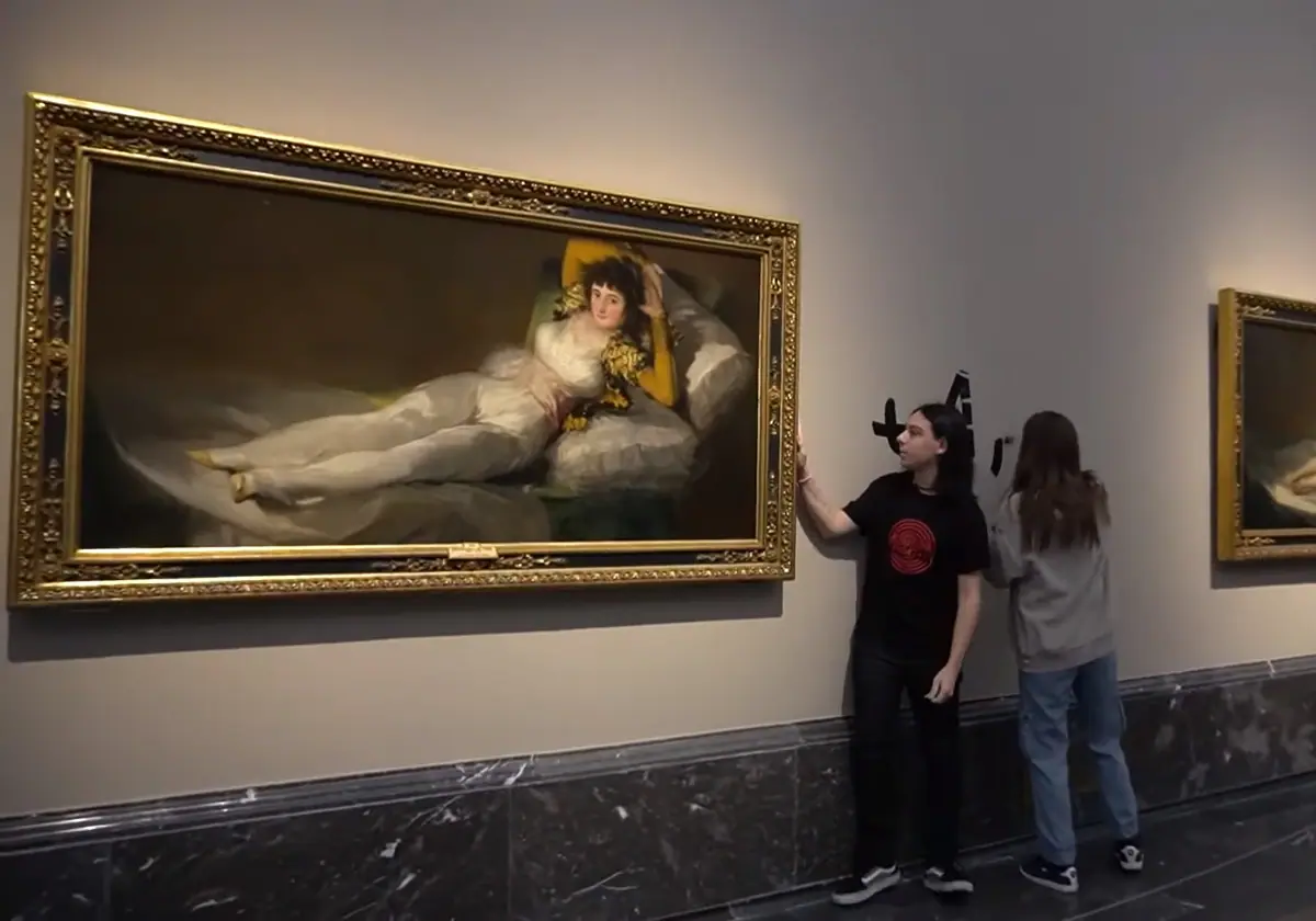 Una activista de Futuro Vegetal se pega al marco de un cuadro de Goya mientras otra hace una pintada en la pared