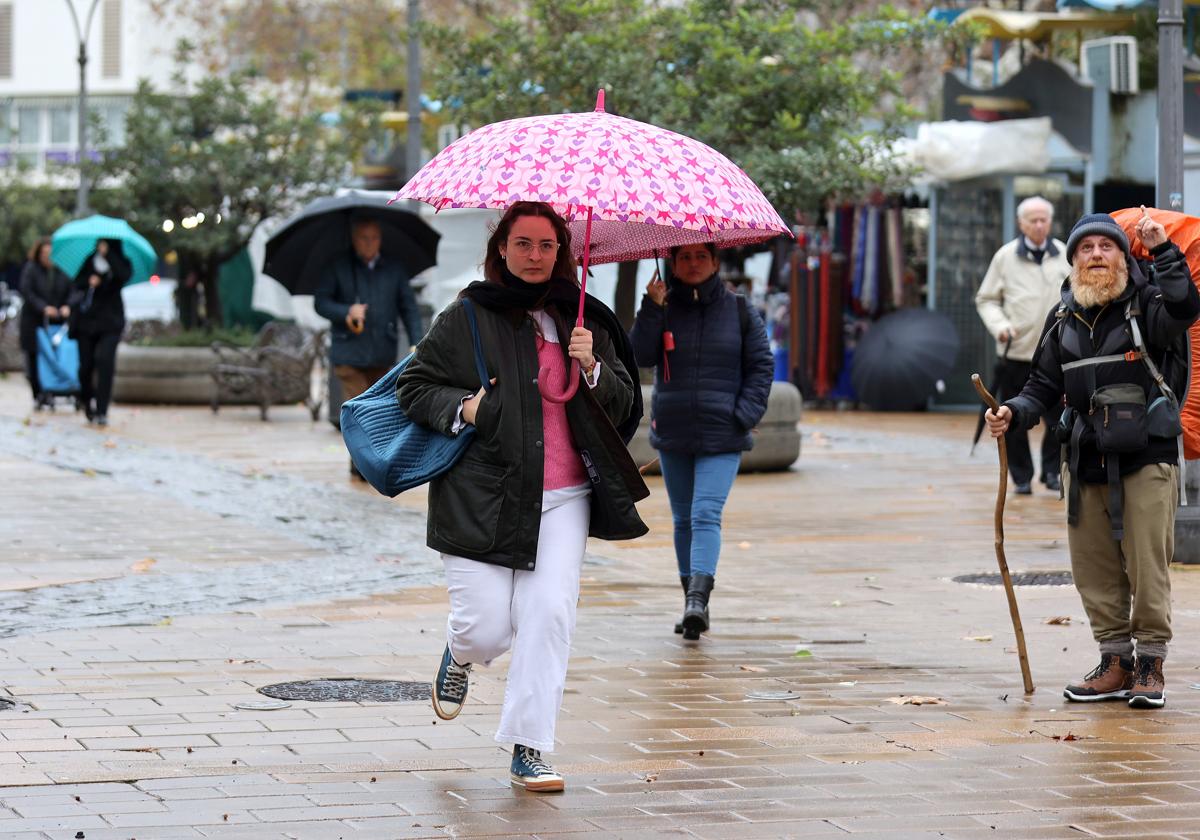 Varias personas atraviesan la Victoria protegiéndose de la lluvia con sus paraguas