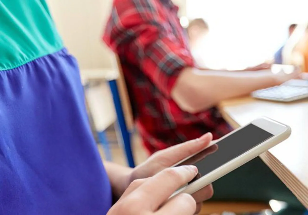 Un menor, con un teléfono móvil en un aula