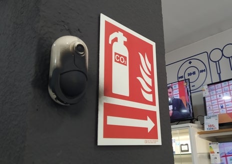 Imagen secundaria 1 - Cristal reventado en la óptica y una cámara de seguridad pulverizada en la tienda de electrodomésticos, donde arracaron una de las pletinas de la puerta trasera de acceso  