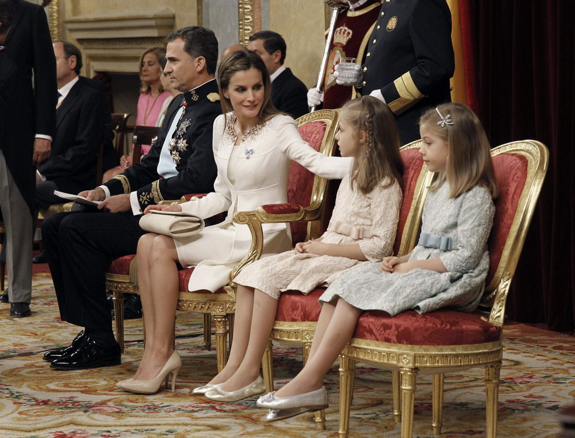 Los Reyes, Don Felipe y Doña Letizia, junto a sus hijas, la Princesa Leonor y la Infanta Sofía, durante el acto de proclamación ante las Cortes Generales. En esta imagen se puede observar a Doña Letizia intercambiando palabras con las menores, momentos antes de dar inicio al discurso de proclamación de Don Felipe como nuevo Rey de la Nación. Los Reyes se sentaron en dos sitiales de honor colocados en la parte central. Las menores se colocaron a la izquierda de sus padres, la Princesa Leonor más cerca de sus padres que la Infanta Sofía.