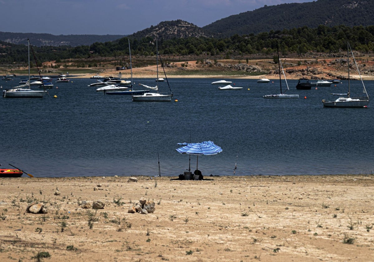 Imagen de archivo de una sombrilla en la playa del embalse de Entrepeñas con las embarcaciones al fondo