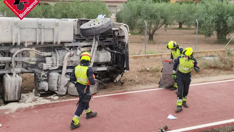 Bomberos junto al camión volcado por la colisión con un coche.