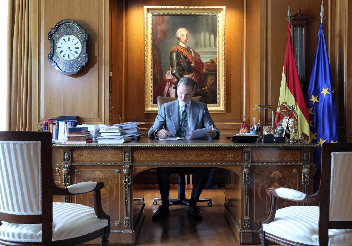 El Rey, trabajando en su escritorio en una foto distribuida por Zarzuela con motivo del décimo aniversario de la proclamación. A su espalda, el retrato de Carlos III y las banderas de España y de la UE