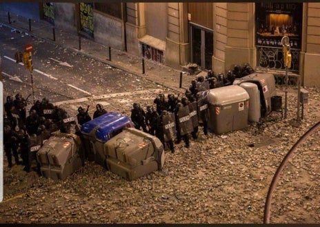 Imagen secundaria 1 - Arriba, los contenedores incendiados de la plaza de Urquinaona. Abajo, los policías (entre ellos Ángel Hernández, defendiendo la comisaría de la Policía Nacional de Vía Laietana. Al lado, un compañero acompaña a Hernández hacia retaguardia mientras anda encogido, doliéndose, camino de la furgoneta.