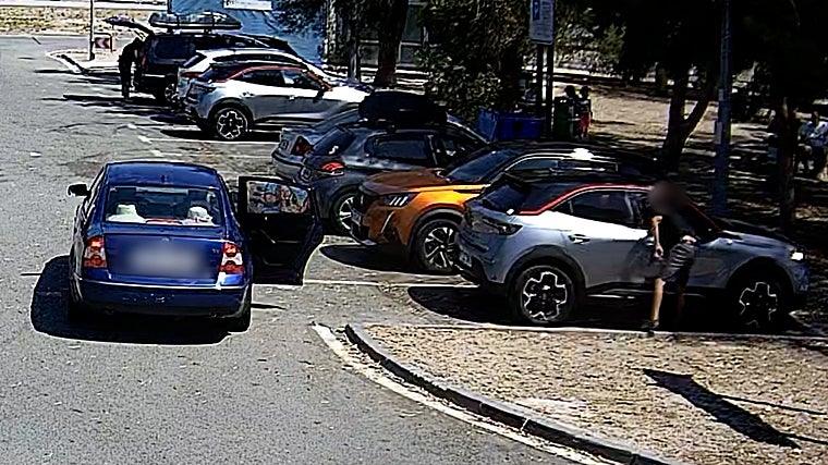 Momento en el que un ladrón roba en un coche aparcado mientras su cómplice espera con su vehículo en marcha para huir.