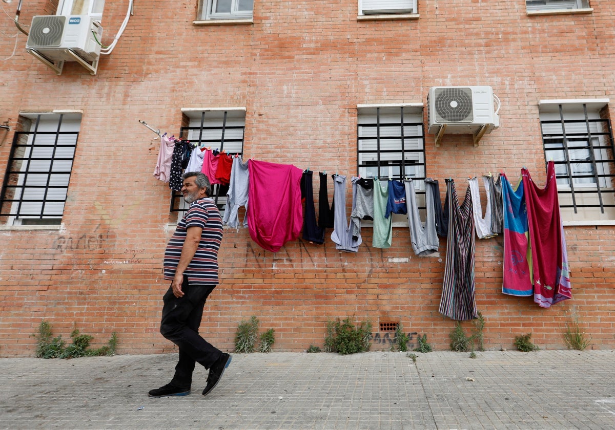 Un vecino camina por la acera en el barrio de Las Palmeras junto a un tendedero de ropa