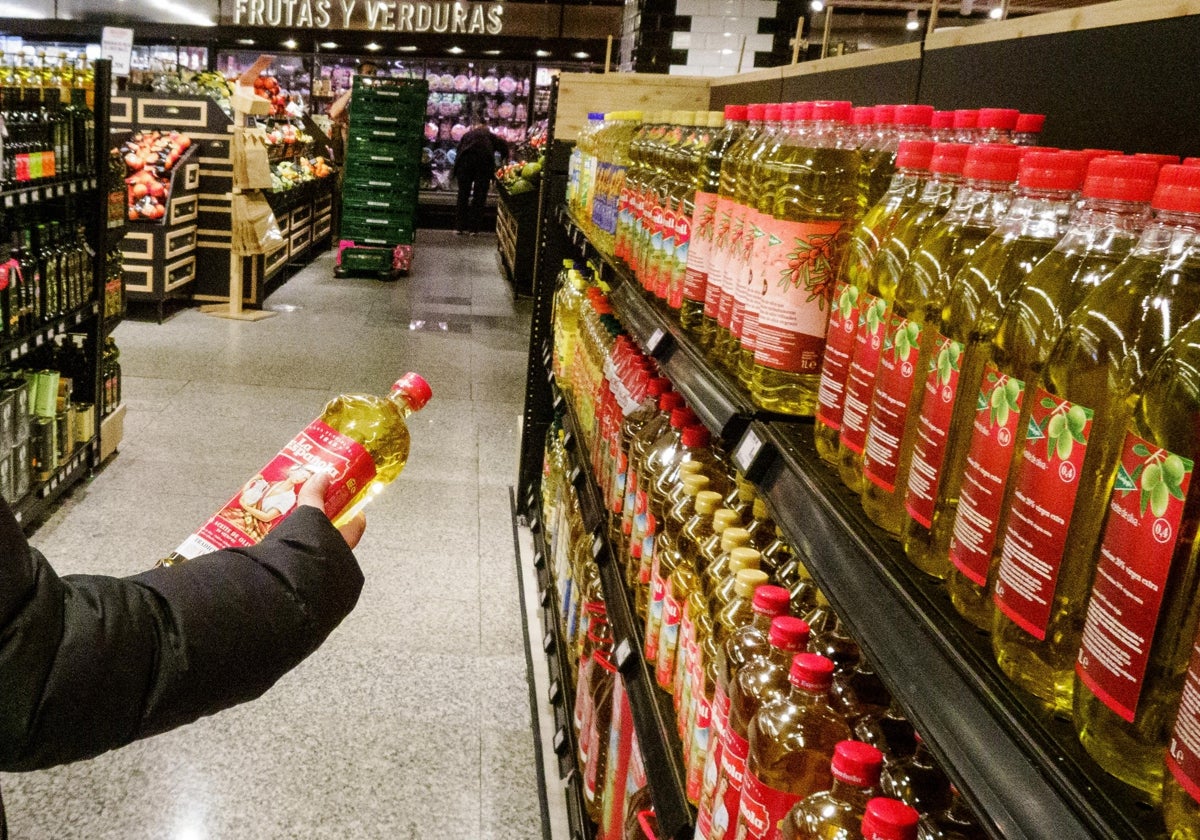 Una mujer observa una botella de aceite de oliva tras cogerla de un lineal en un supermercado