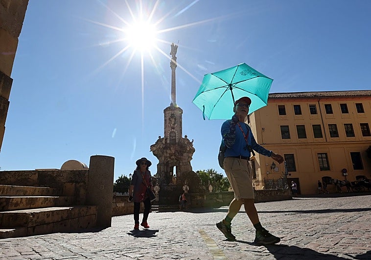 Turistas pasean alrededor de la Mezquita Catedral de Córdoba protegidos del sol con paraguas y sombreros