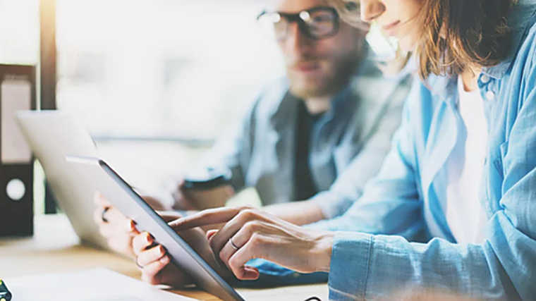 Imagen de archivo de dos personas usando una tablet y un ordenador