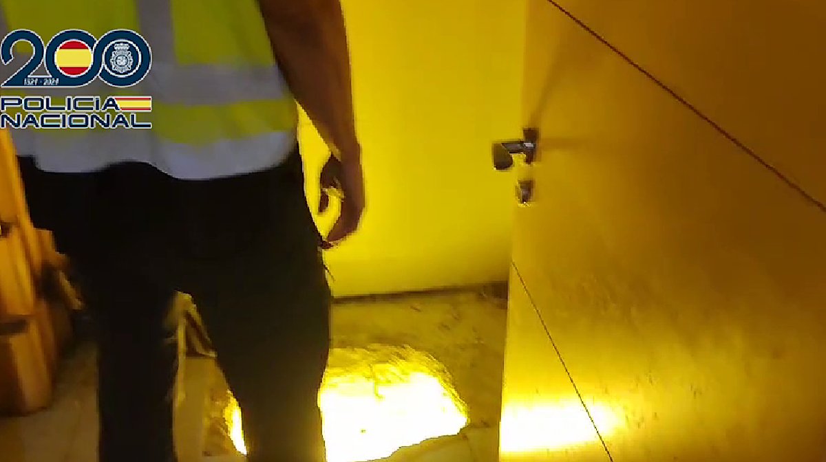 Imagen de un policía ante la entrada secreta de un cultivo de marihuana en un chalet de Valencia