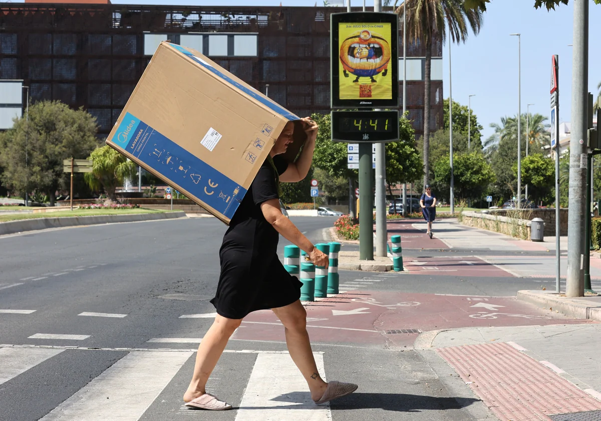 Un joven cruza una avenida de Córdoba protegido por un cajón ante el calor