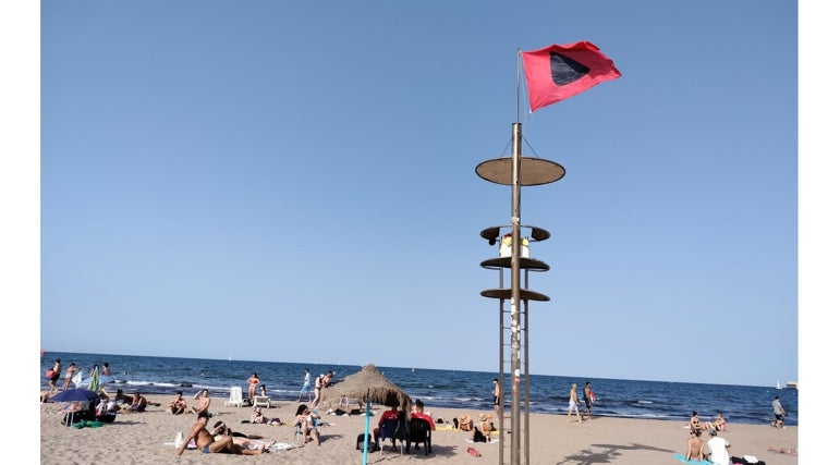 Imagen de la bandera roja en el tramo afectado por las algas en la playa del Cabanyal