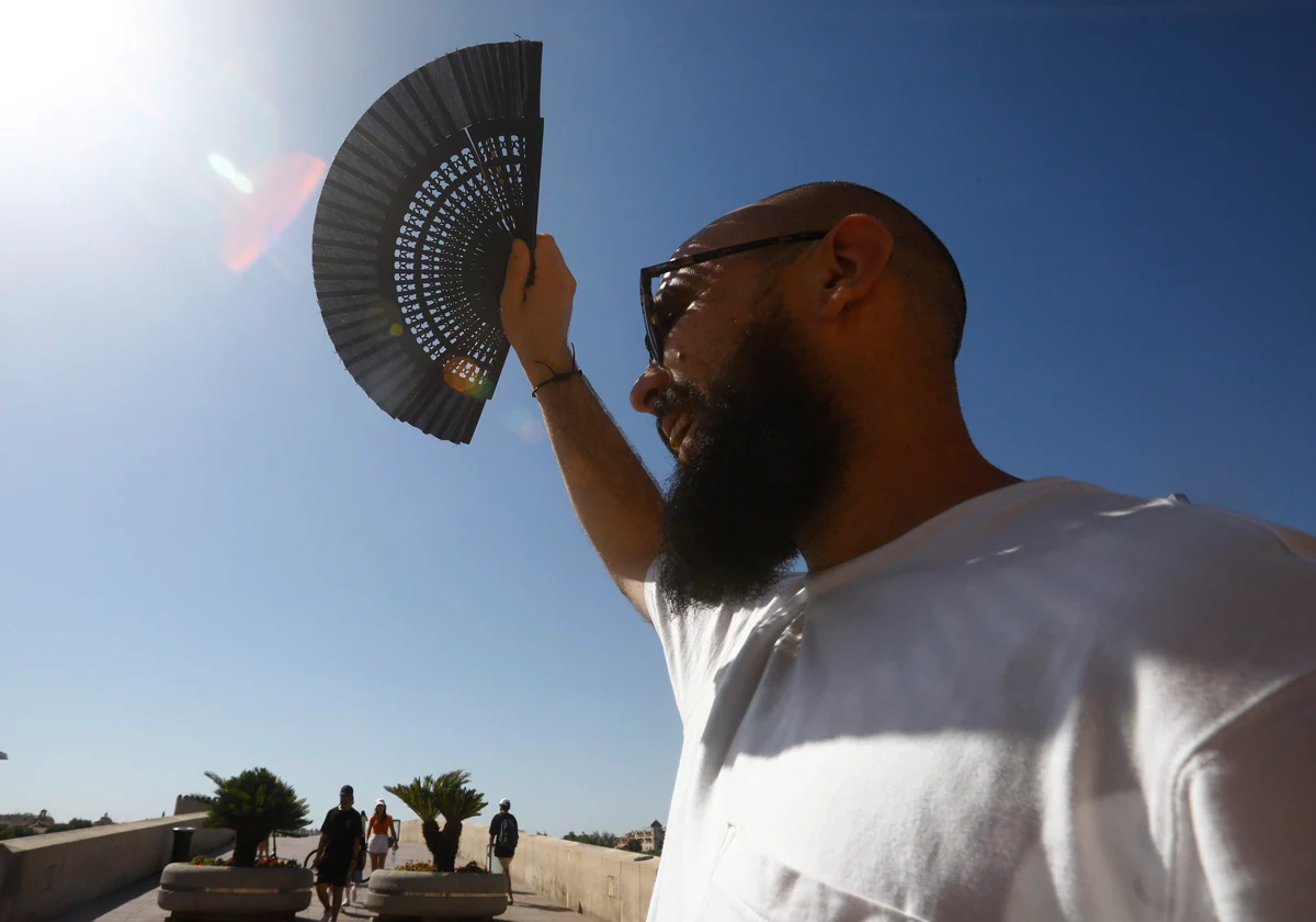 Un hombre tapa el sol con un abanico junto al Puente Romano de Córdoba