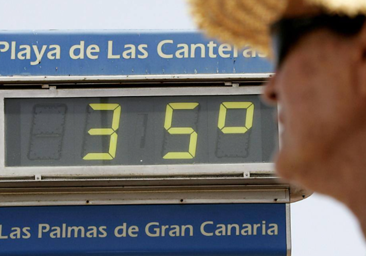Una mujer se protege del calor junto a uno de los termómetros de la playa de Las Canteras, en Gran Canaria
