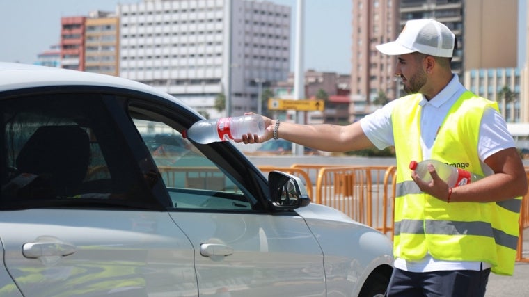 Un auxiliar entrega una botella de agua a los ocupantes de un vehículo en el puerto de Algeciras