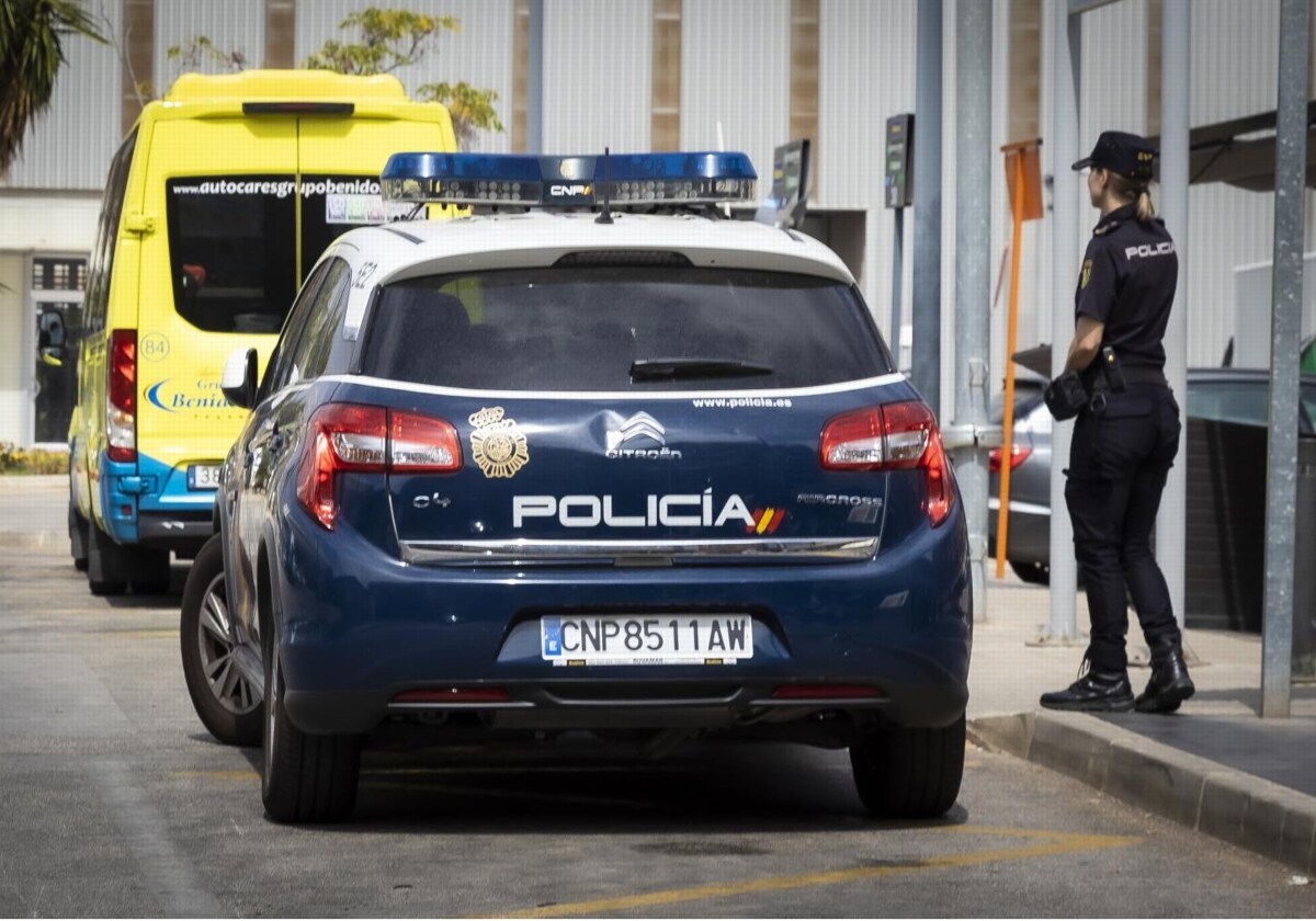 Una agente de la Policía Nacional junto a un coche patrulla y una ambulancia