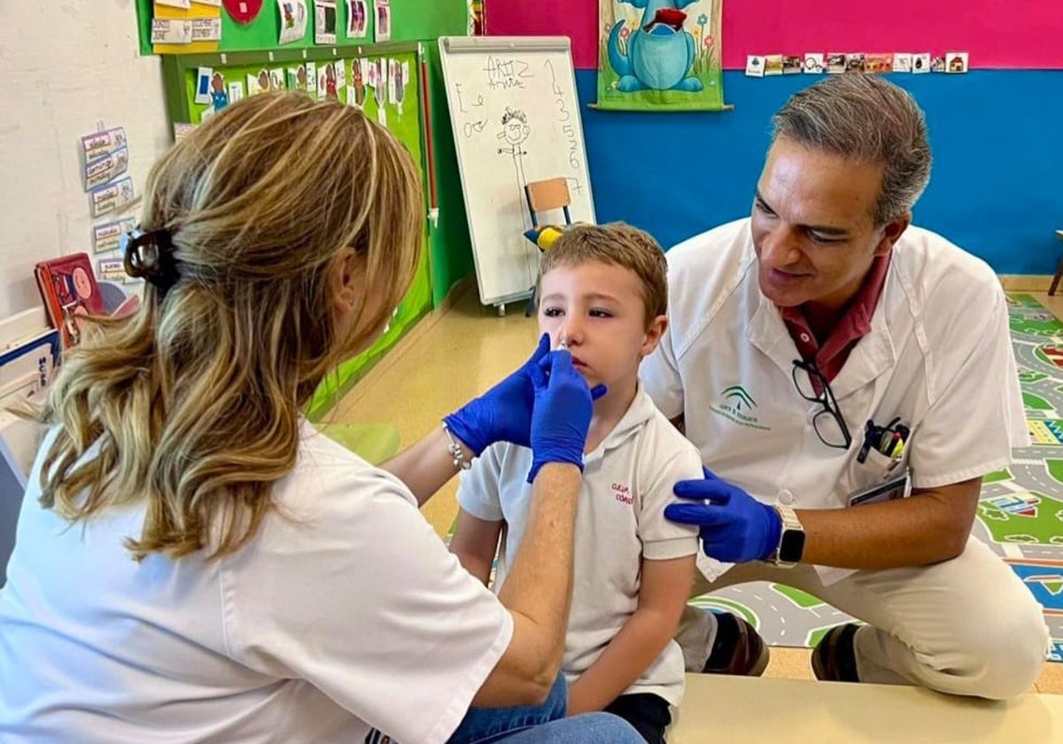 dos enfermeros vacunan de la gripe a un escolar en el colegio Colón vía intranasal