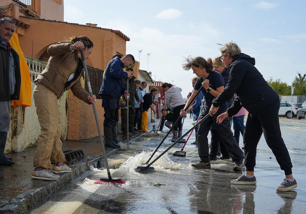 Varios vecinos de la calle Buen Pastor, de San Fernando, barren el agua a la alcantarilla