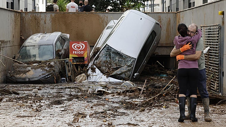 Dos vecinos se abrazan a la entrada de un garaje en Paiporta, Valencia, tras el paso de la DANA