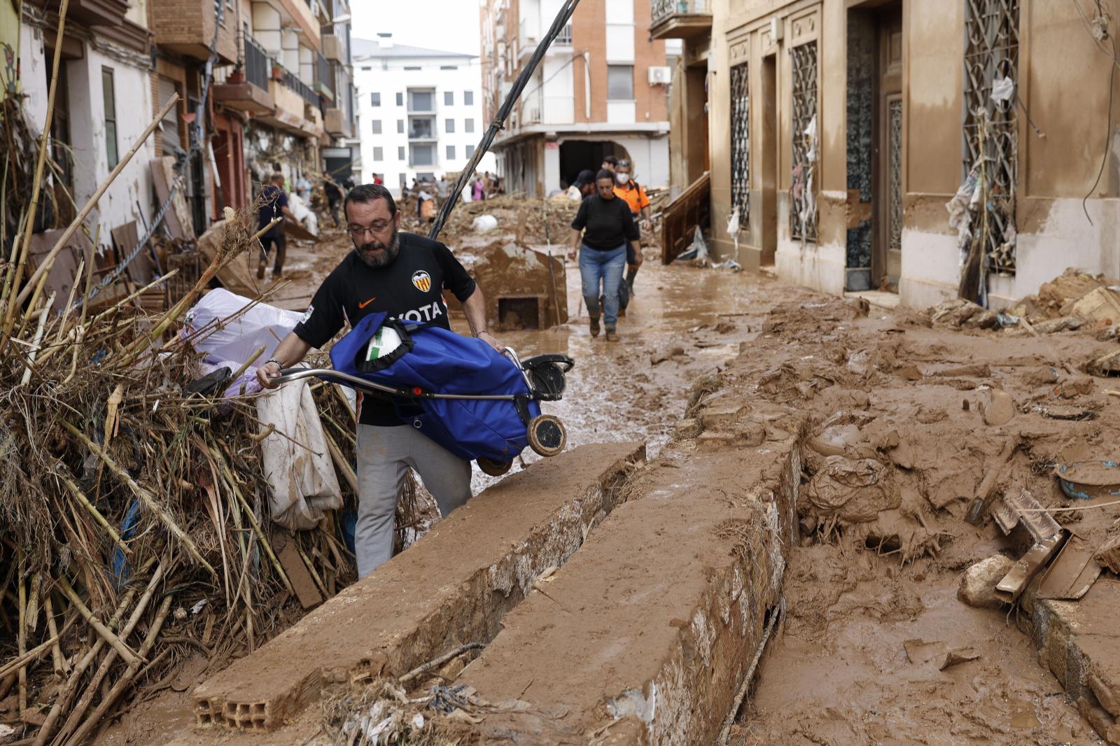 Un vecino lleva en volandas un carro de la compra entre el fango y escombros en la localidad de Paiporta tras el paso de la DANA