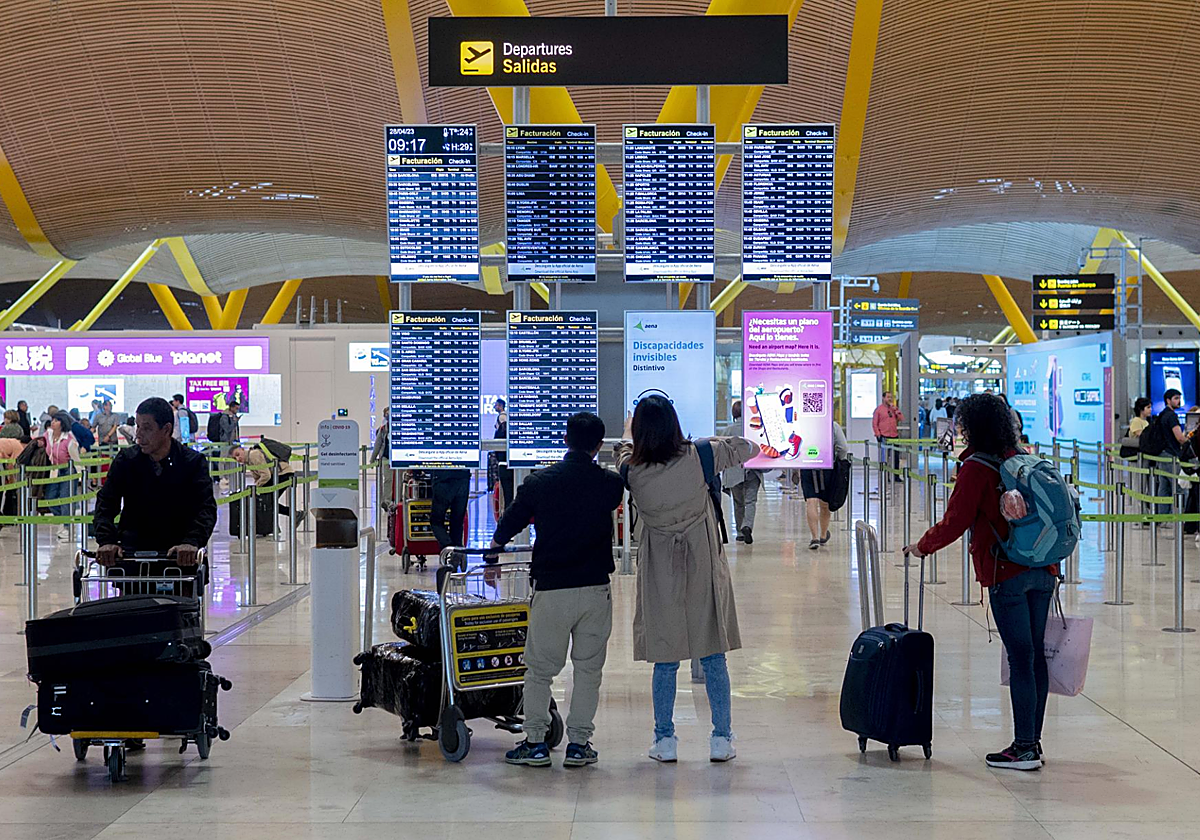Un grupo de personas frente al panel del orden de vuelos en la terminal T4 del aeropuerto de Adolfo Suárez-Madrid Barajas