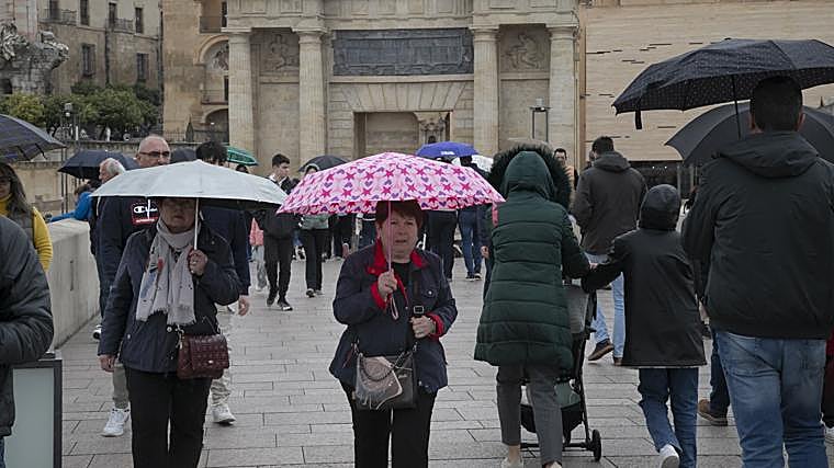 Turistas se protegen de la lluvia mientras pasean por el Puente Romano
