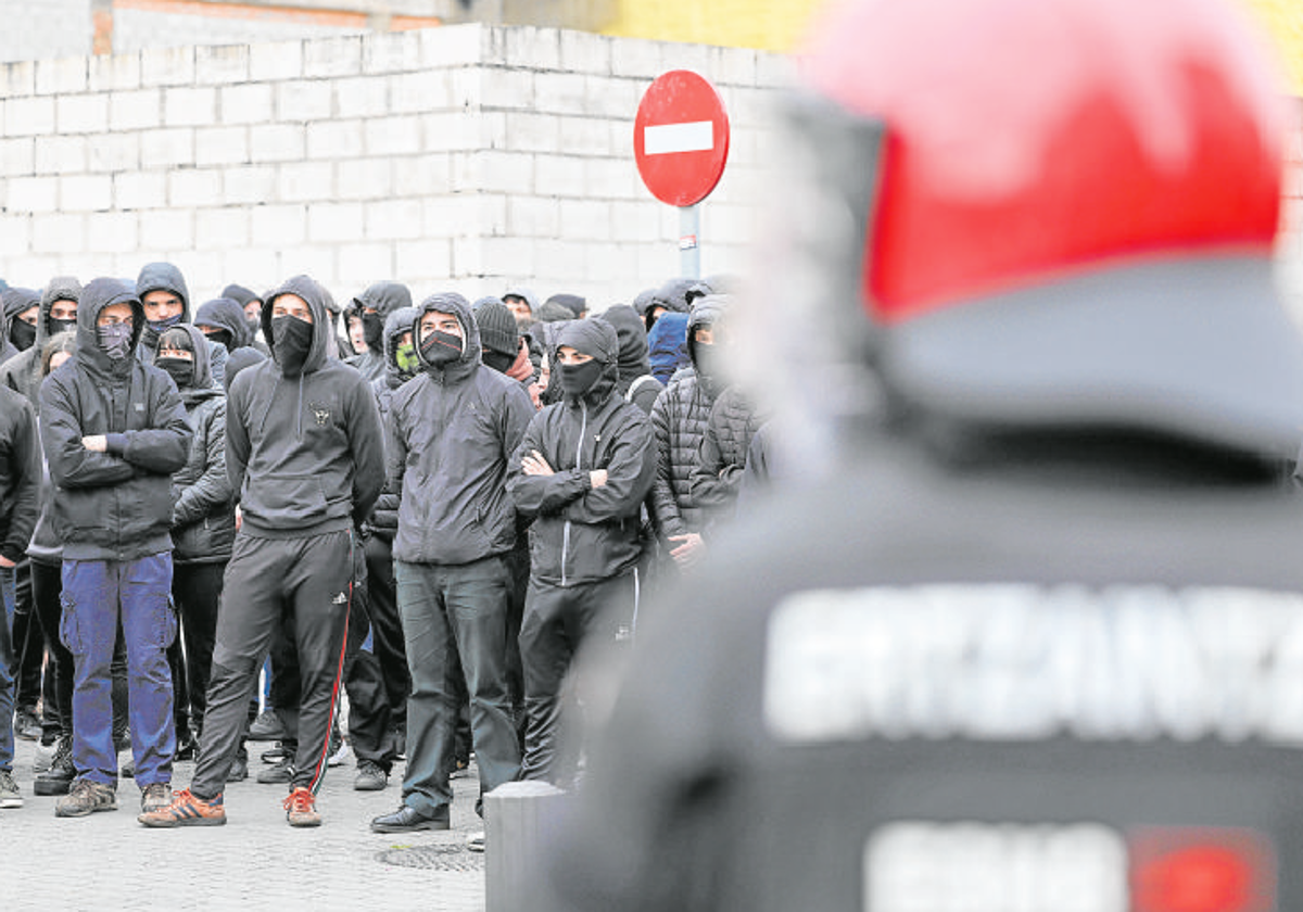 Un grupo de jóvenes embozados espera frente a efectivos antidisturios de la Ertzaintza