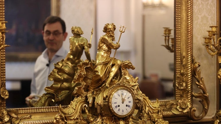 El relojero Alberto Barba en el reflejo del espejo que hay tras uno de los relojes que repara