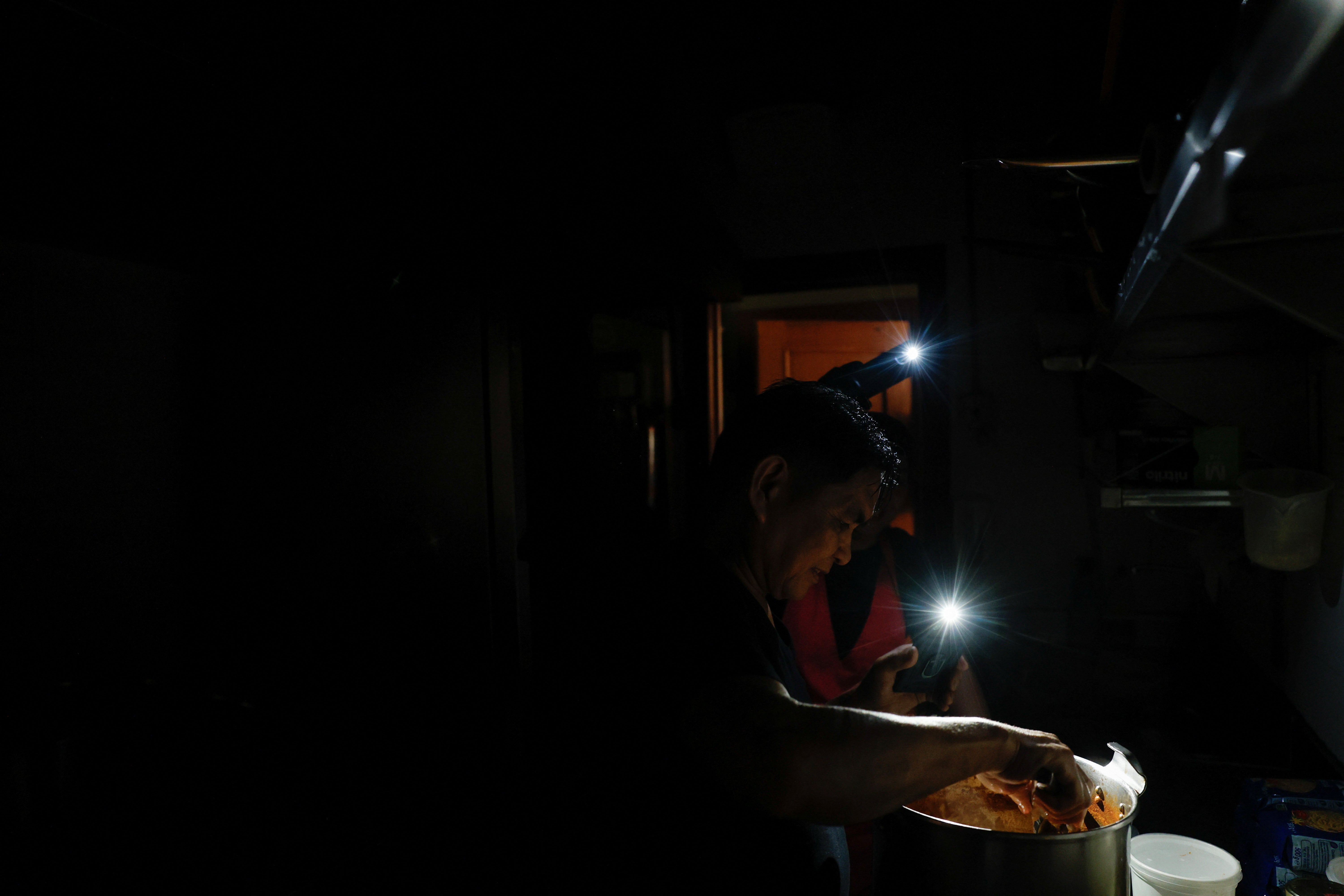 Una persona cocinando a la luz  de las linternas del móvil.
