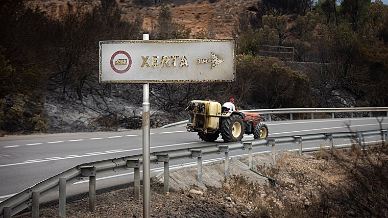 Un campesino en su tractor, ante el cartel quemado del municipio de Xerta