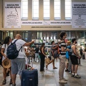 Viajeros, esperando en la estación de Santa Justa, con el polémico cartel al fondo.