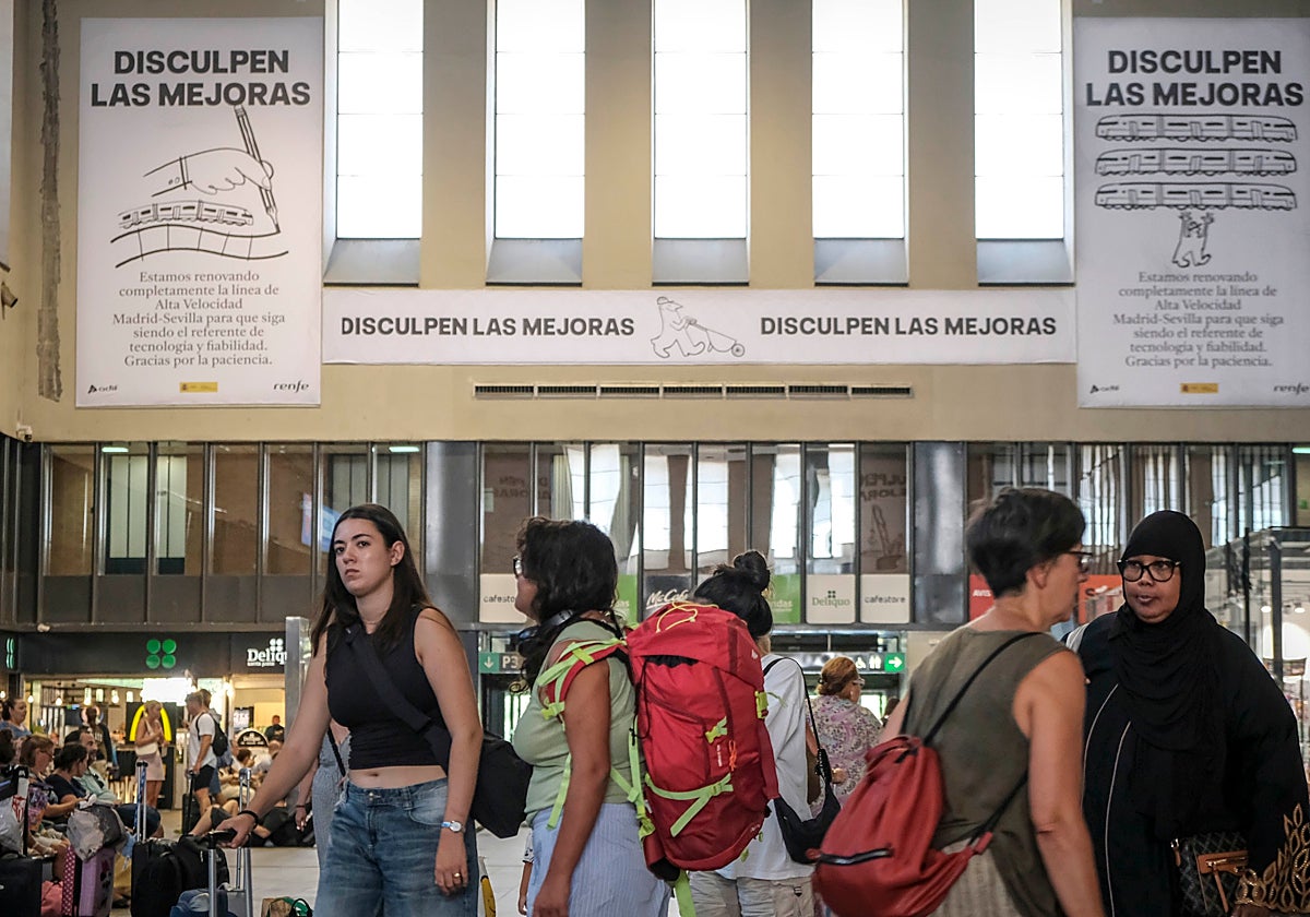Viajeros en Santa Justa con los carteles de la campaña del Gobierno de fondo