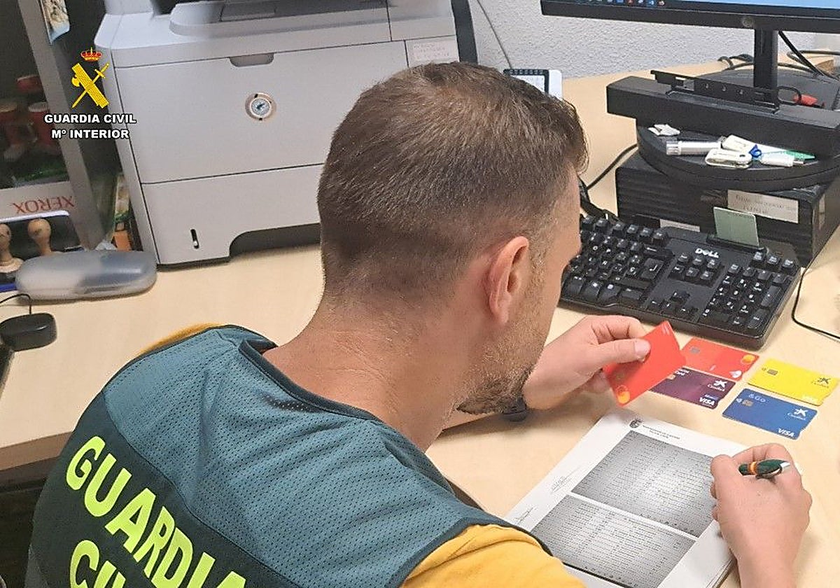 Imagen de un agente de la Guardia Civil cotejando el registro de ingresos del detenido con las tarjetas robadas