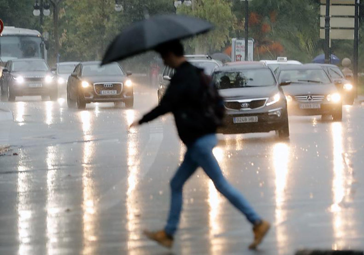 Imagen de una persona cruzando un paso de cebra un día de lluvia en Valencia