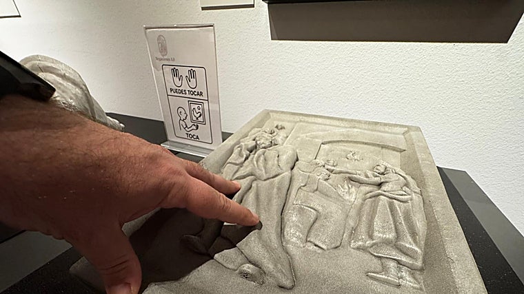 Una mano toca el relieve táctil de la exposición