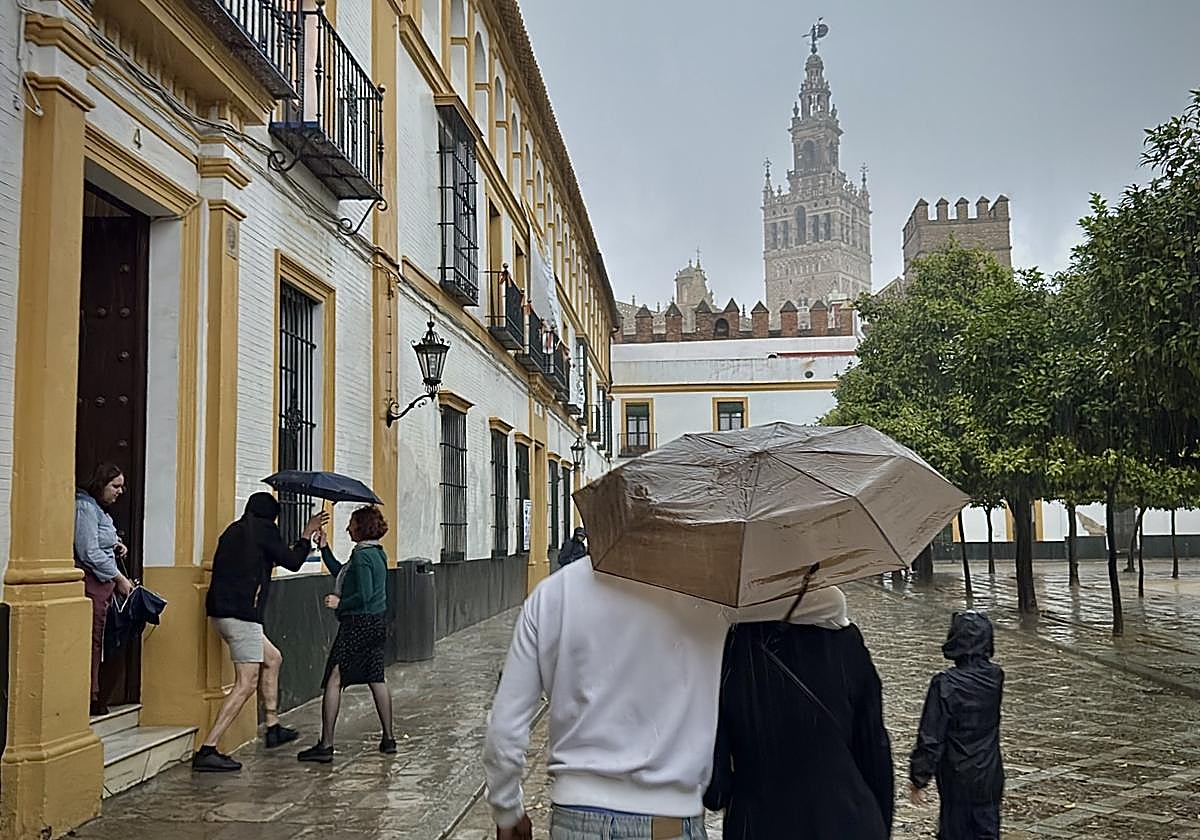 Varias personas se resguardan de la lluvia por una calle de Sevilla